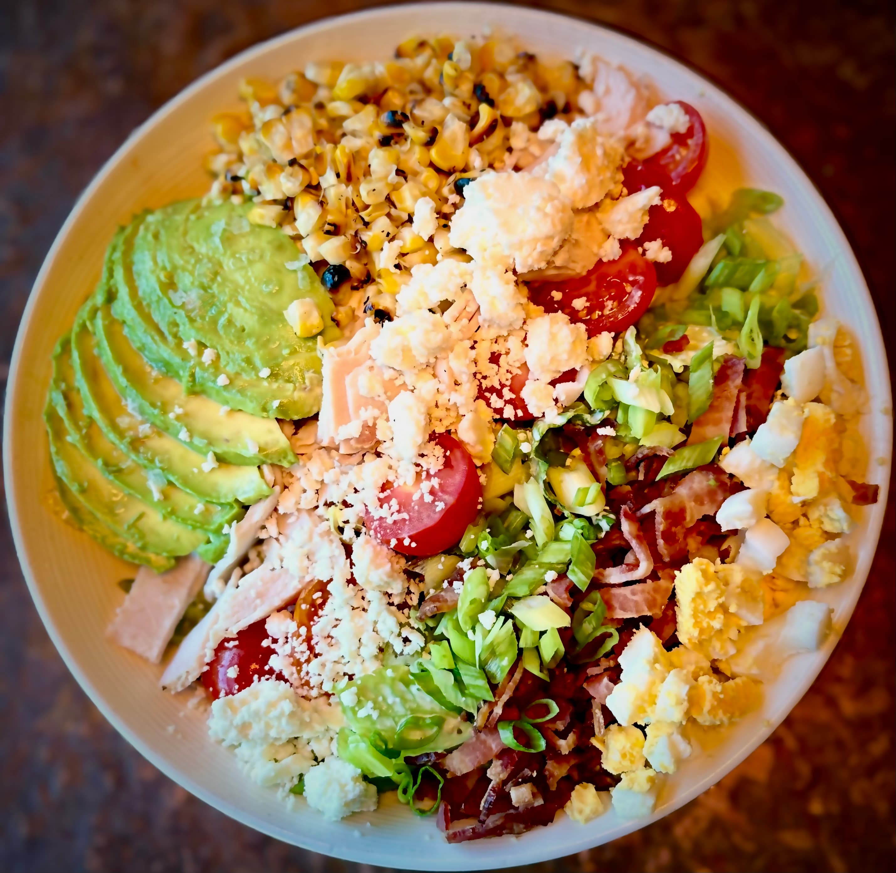 A Cobb-style salad with turkey, avocado, charred corn, tomato, bacon, egg, scallions, and crumbled cheese