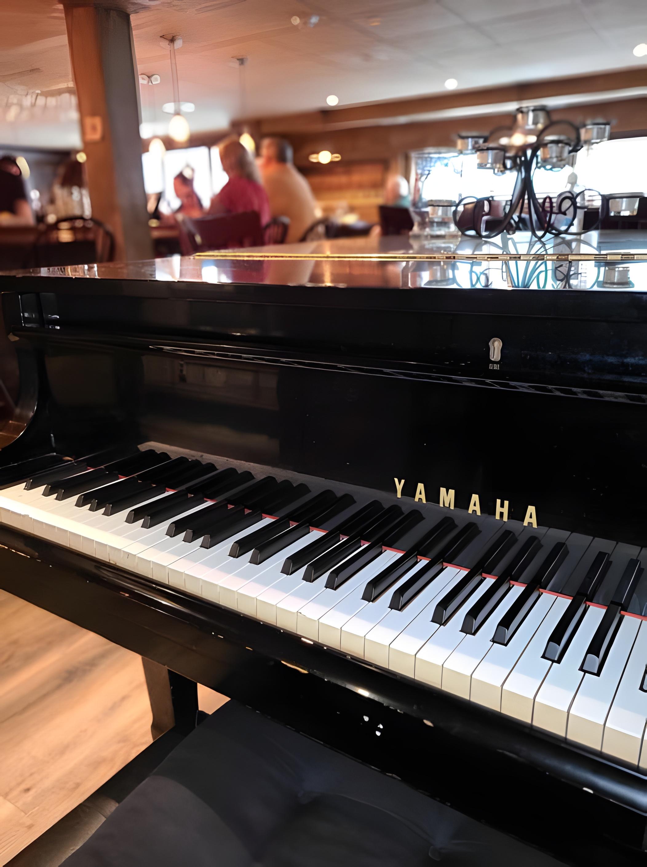 The grand piano in Bowman's dining room, guests seated in the warm-lit room beyond.